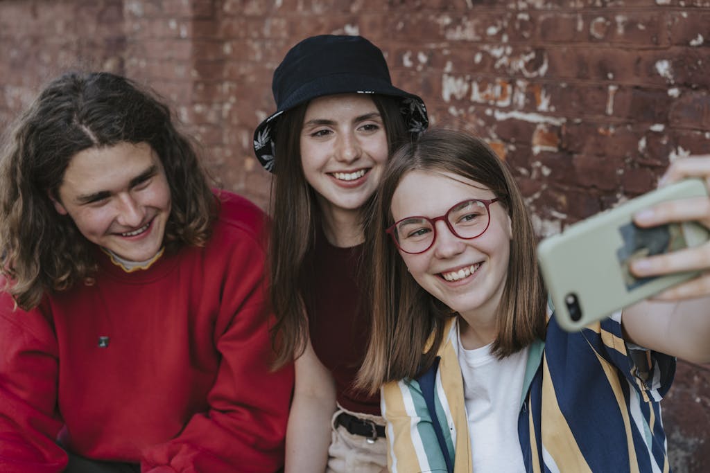 A group of happy teenagers taking a selfie outdoors against a brick wall.